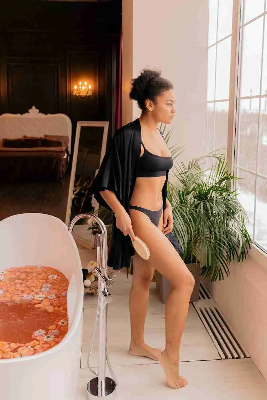 woman dry brushing her body and standing next to a flower bath