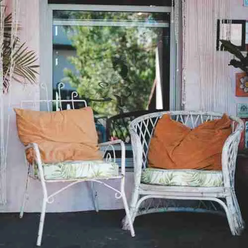 Comfortable wicker chairs with pillows placed on rural house terrace near window and potted houseplants on sunny day